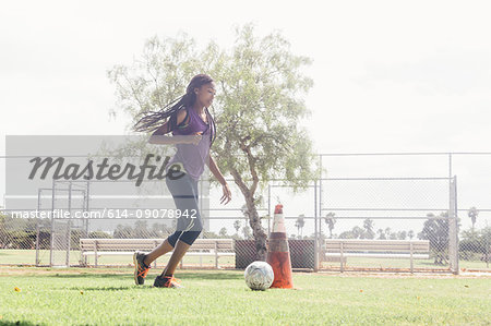 Teenage schoolgirl doing dribbling soccer ball practice on school sports field