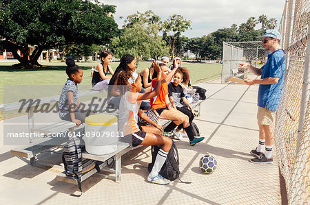 Teacher questioning schoolgirl soccer players on school sports field bench