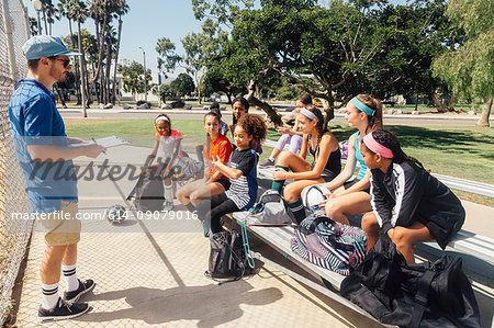 Teacher instructing schoolgirl soccer players on school sports field bench