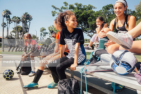 Schoolgirl soccer players chatting on school sports field bench