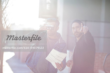 Two men in street, mid adult man looking through camera, young man pointing ahead