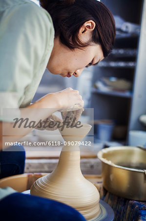 Woman working in a Japanese porcelain workshop, sitting at a potter's wheel, throwing bowl.