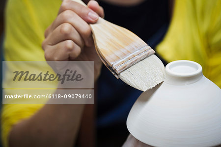 Close up of person working in a Japanese porcelain workshop, glazing white bowls with paintbrush.