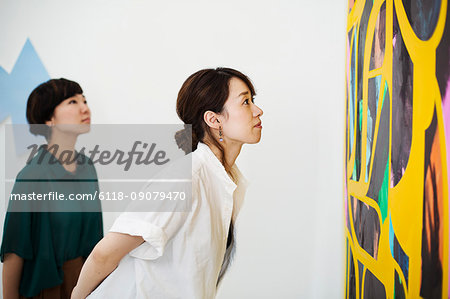 Two women standing in an art gallery, looking at an abstract modern painting.