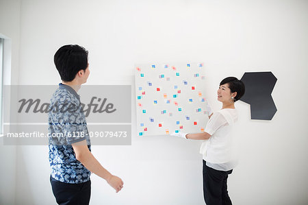 Man wearing blue shirt watching woman hang modern painting on white wall in art gallery.