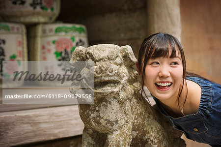 Young woman wearing blue dress standing next to stone sculpture of lion at Shinto Sakurai Shrine, Fukuoka, Japan.