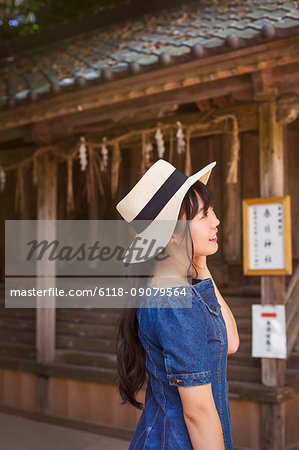 Young woman wearing blue dress and hat standing at Shinto Sakurai Shrine, Fukuoka, Japan.