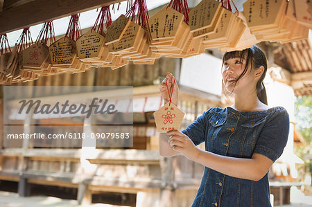 Young woman wearing blue dress looking at wooden fortune telling plaques at Shinto Sakurai Shrine, Fukuoka, Japan.