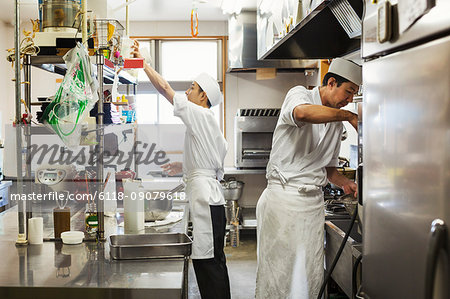 Two chefs working in the kitchen of a Japanese sushi restaurant.