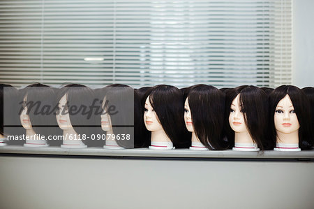 Large group of mannequin heads with brown wigs in a row on a table.