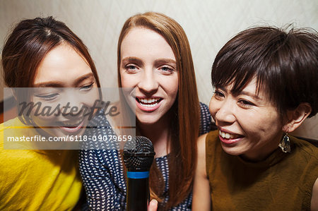 Three people, two women and man, holding microphone, singing, making music.