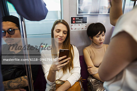 Three people sitting sidy by side on a subway train, Tokyo commuters.
