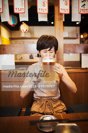 Woman sitting at a table in a restaurant, drinking from large glass of beer.