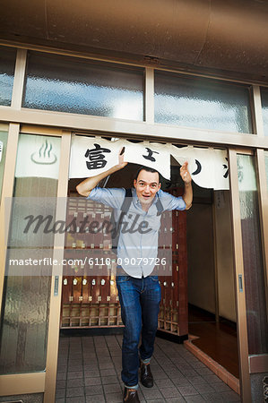 A young Western man coming out of a public bath house, ducking under the entrance sign.