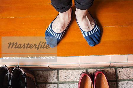 A man's feet in socks by a row of shoes.