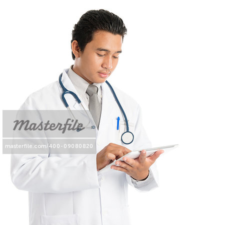 Portrait of attractive young male Southeast Asian medical doctor using tablet pc, standing isolated on white background.