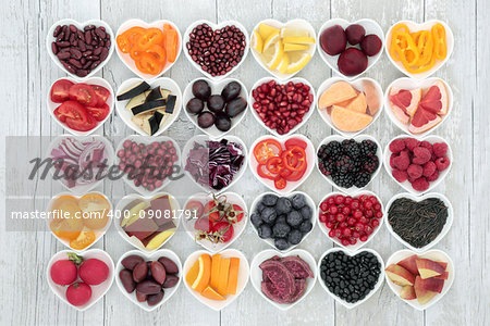 Food for healthy living with fruit, grains, vegetables and pulses in heart shped dishes on rustic wood background. Health foods high in antioxidants, anthocyanins, vitamins and minerals.