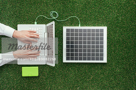 Man working with a laptop on the grass connected to a solar panel, alternative energy sources and electrical power generation concept