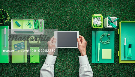 Businessman using a digital tablet on a grass desktop; green business, technology and communication concept