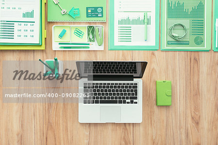 Laptop, green office supplies and financial reports on a wooden desktop, green business and ecology concept