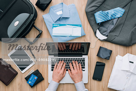 Corporate businessman packing his bag and planning a business trip, he is booking flights online using a laptop, travel and technology concept