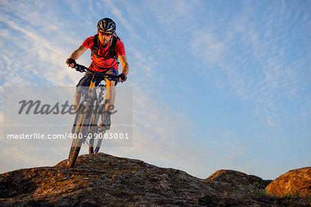 Cyclist in Red T-Shirt Riding the Bike Down the Rock on the Blue Sky Background. Extreme Sport and Enduro Biking Concept.