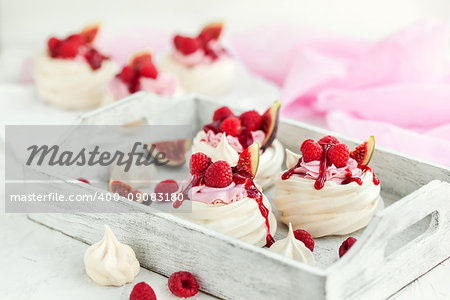 Delicious mini Pavlova meringue cake decorated with fresh raspberry, figs  and berry sauce on white background