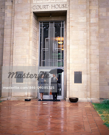 1990s COUPLE OUTSIDE OF COURTHOUSE IN THE RAIN WITH UMBRELLAS