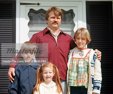 1970s SINGLE FATHER WITH HIS ARM AROUND HIS CHILDREN LOOKING AT CAMERA STANDING BY FRONT DOOR OF HOUSE