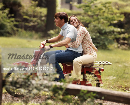 1960s 1970s YOUNG TEENAGE COUPLE RIDING ON MOTORBIKE BOY DRIVING GIRL HOLDING ON BEHIND LAUGHING