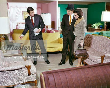 1960s COUPLE WITH SALESMAN LOOKING AT SHOWROOM FURNITURE IN DEPARTMENT STORE NOSTALGIA TUFTED MAN WOMAN
