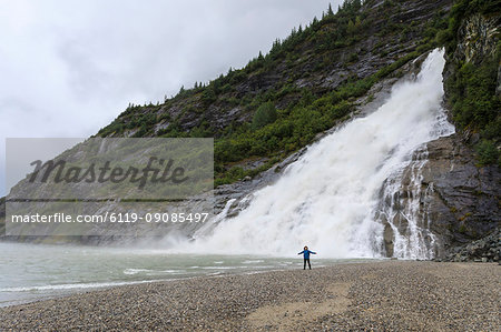 Visitor with outstretched arms on a beach in front of Nugget Falls Cascade, Mendenhall Lake and Glacier, Juneau, Alaska, United States of America, North America