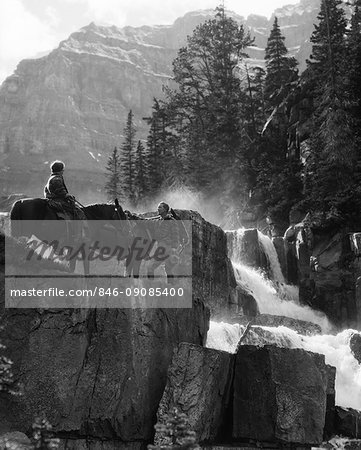 1930s COUPLE WOMAN ON HORSE MAN STANDING BY HORSE NEAR WATERFALL IN PINE FOREST GIANTS STEPS PARADISE VALLEY ALBERTA CANADA