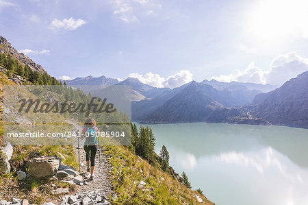 Hiker on path towards Rifugio Bignami beside the dam and water basin of Alpe Gera, Malenco Valley, Valtellina, Lombardy, Italy, Europe