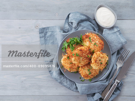 Close up view of potato pancakes. Potato flapjack on gray plate over gray wooden table, with fresh parsley and sour cream. Copy space for text. Top view or flat-lay.