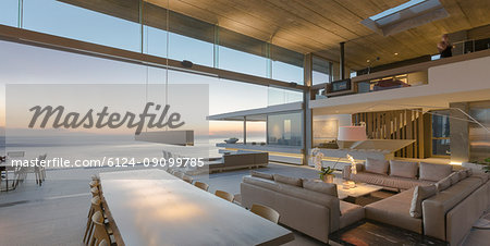 Modern, luxury home showcase living room and dining room open to ocean view at dusk