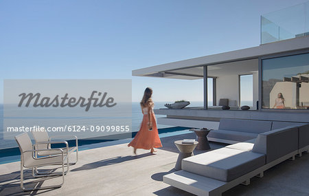 Woman in dress walking on sunny, modern, luxury home showcase exterior patio with ocean view