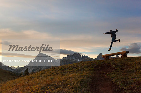 A hiker jumps in fornt of Lagazuoi, Dolomites, Cortina d'Ampezzo, Belluno province, Veneto, Italy