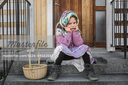 Pensive girl dressed up as Easter witch with Easter basket sitting on steps