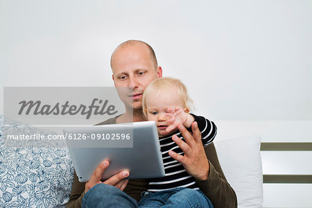 Stay at home dad using tablet while holding baby son
