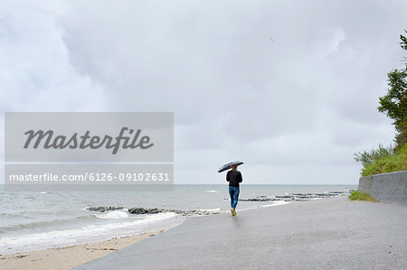 Woman under black umbrella walking on beach