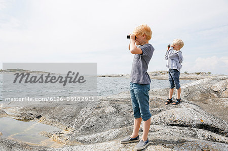 Two boys looking through binoculars on rocky seashore in the Stockholm archipelago