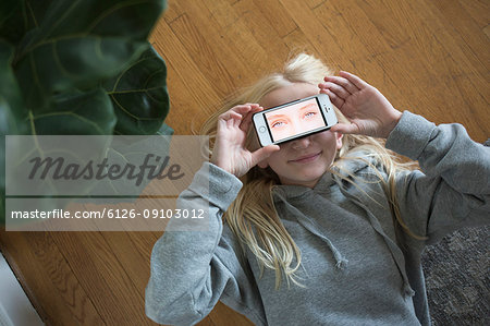 Girl lying on floor and covering eyes with smart phone with eyes on screen