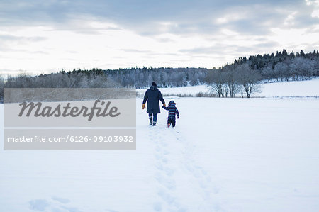 Rear view of mother and child walking in snow