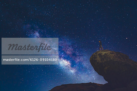 Man standing on rock in Joshua Tree National Park and looking at Milky Way