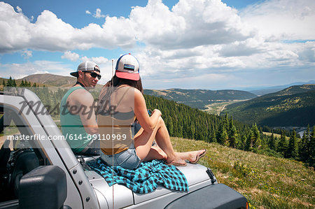 Road trip couple sitting on car hood in Rocky Mountains, Breckenridge, Colorado, USA