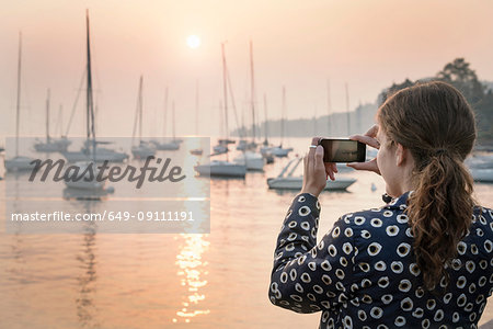 Rear view of woman photographing boats at sunset, Lazise, Veneto, Italy, Europe