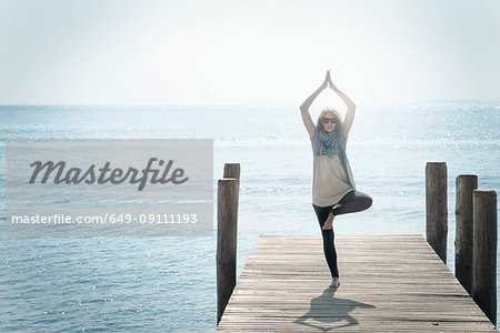 Woman on pier balancing on one leg in yoga pose