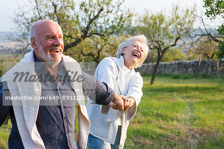 Senior couple walking in rural setting, holding hands, fooling around