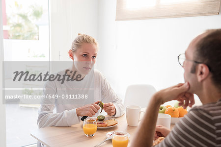 Young woman and boyfriend peeling kiwi fruit at breakfast table